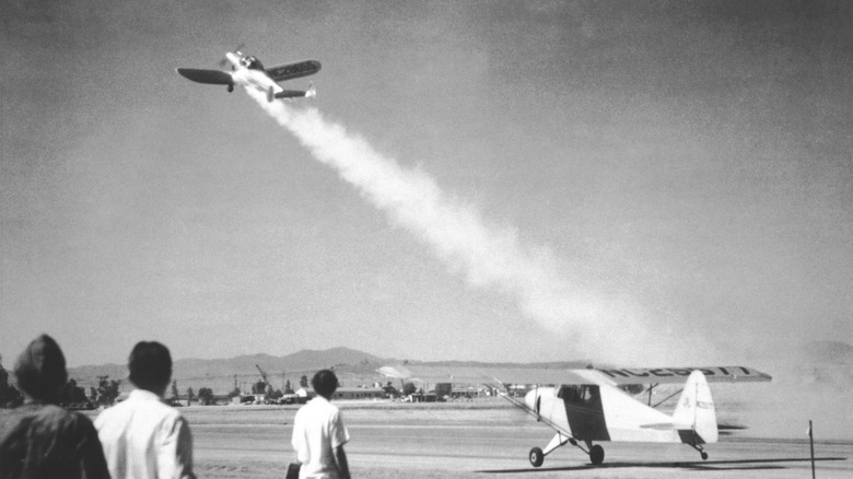 An Ercoupe climbing steeply on a plume of rocket exhaust at March Field while a second Ercoupe waits on the runway