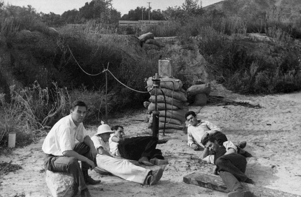 Five young men lounging beside a sandbagged rocket test stand in the dry wash of the Arroyo Seco
